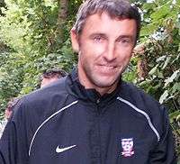 A man with dark hair who is wearing a light blue top and white shorts.