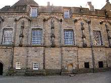 The side of a stone building with windows and figures on pedestals.