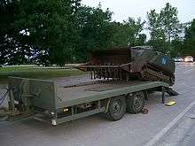 A self-propelled machine being loaded onto a vehicle transportation trailer