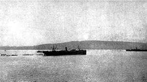 Two ships lying offshore, surrounded by small boats