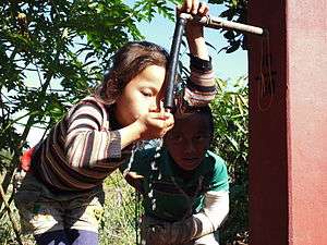 Two children drink from a tap stand.