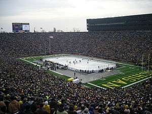 A hockey rink is set up in the middle of a football field, with thousands of people surrounding the playing surface