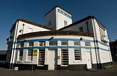 A white brick building with two horizontal blue stripes, and a rounded quarter-circle frontage