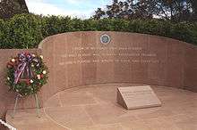 A paneled, marble wall decorated with a seal and some inscribed words. A plaque with name and dates rests on the shiny marble floor.