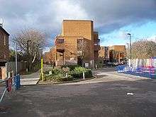 A footpath stretches in a straight line into the distance, next to a large yellow rectangular building