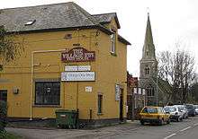 An orange walled building with a church spire behind it