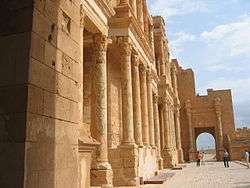 A side view of a large building to the right, with stone, cylindrical pillars running along its front.