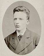 Head shot photo of a young man, similar in appearance to his brother, but neat, well-groomed and calm.