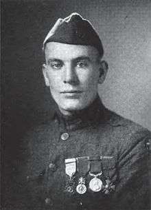 Head and shoulders of a clean cut man in military uniform with four medals hanging from ribbons on his chest and a garrison cap.