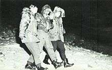 Black and white photograph of an airman in a bomber jacket being assisted to walk by two men