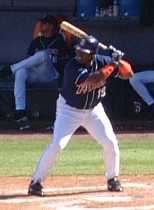 A man in a blue batting helmet and baseball uniform stands in a left-handed batting stance.