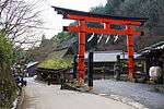 Large red torii next to a wooden thatched house.