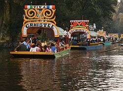 Roofed barges with many people on a canal.