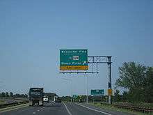 A divided highway curves to the left as the rightmost lane exits underneath an overhead green sign indicating the ramp leads to Worcester Highway and MD 589 toward Ocean Pines