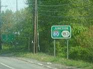 A green sign on the side of a wooded road reading junction Interstate 80/Route 183