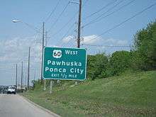 A large green road sign, reading "US-60 West/Pawhuska, Ponca City/Exit ½ Mile"