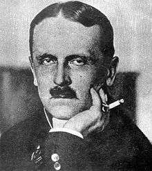 A man, smoking, poses for a portrait photograph.