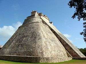 Stone pyramid with smooth surfaces and rounded corners. A staircase on one side leads to a structure at the top of the pyramid.