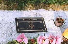 a bronze plaque headstone set in a block of concrete amongst grass, with flowers in the foreground