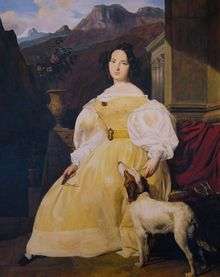 A woman with short black hair arranged in curls is wearing a yellow dress. She is seated with one hand resting on a dog's head, the other holding a pair of glasses.