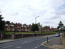 A row of small redbrick cottages with exuberant decoration to the gable ends. A central stone built hall.