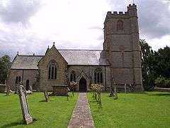 Stone church with square tower. In the foreground are a path and gravestones