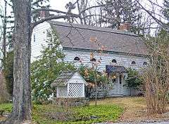 A white wooden house with a gambrel roof, two brick chimneys and semicircular windows