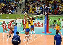 Brazilian and Cuban athletes during a volleyball match wearing the official uniforms of their respective nations. The audience remained watching at the competition venue for the volleyball tournament.