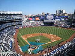 A baseball stadium with blue seats and buildings visible in the background.