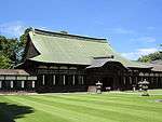 Wooden building with a hip-and-gable roof and attached canopy with Chinese style gable. On either side, the building is connected to a wooden corridor.